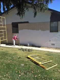 a woman standing in front of a house next to a yellow ladder and some green grass