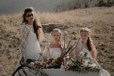 two women in white dresses standing next to a table with flowers and plants on it