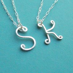 two silver initial necklaces with the letter k on each one, sitting on a blue surface