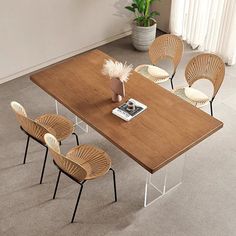 a wooden table with four chairs and a book on it in a living room next to a potted plant