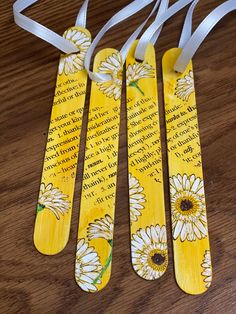 three yellow bookmarks with white daisies on them sitting on a wooden table next to a ribbon