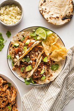 two plates filled with shredded meat and tortillas next to bowls of salsa, lime wedges and sour cream