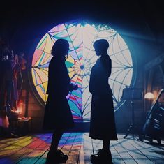 two women standing in front of a stained glass window with lights coming from it and one woman holding an umbrella