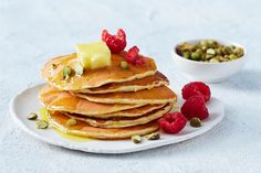 a stack of pancakes on a plate with raspberries and pistachio