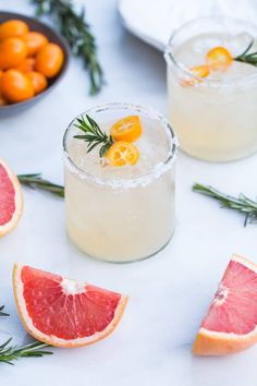 two grapefruit cocktails with rosemary garnish on the rim and orange slices