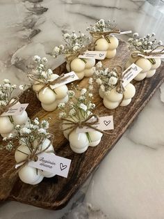 small white vases filled with flowers on top of a wooden board