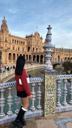 a woman is standing on a bridge looking at the water and building in the background