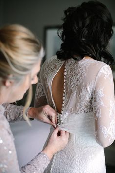 a woman in a white dress is helping another woman put on her wedding dress with pearls