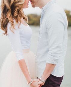 a man and woman standing next to each other in front of a body of water