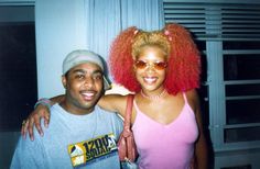 a man standing next to a woman in a pink shirt and red afro wig on her head