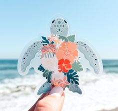 a person holding up a sticker with flowers and an ocean in the back ground