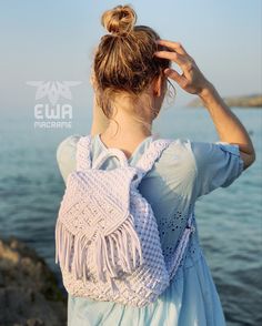 a woman is standing by the water with her hair in a bun and wearing a crocheted bag