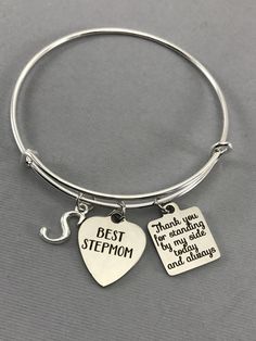 Best Stepmom charm bangle bracelet with a marriage charm and initial. Features: Adjustable Bangle Bracelet, Silver Plated Measures 61mm The initial charm is made from a zinc alloy metal which is lead and nickel free. Measurements: 14mm x 16mm Best Stepmom and Thanks for standing by my side today and always charm are made of stainless steel Measurements: 19mm x 22mm Each purchase will arrive packaged in a cute kraft gift box ready to give as a present or a fun gift for yourself! Add on a birthsto Personalized Charm Bracelet For Bridesmaid Gift On Mother's Day, Personalized Charm Bracelet For Bridesmaids, Engraved Charm Bracelet For Mother's Day Personalized Gift, Adjustable Stainless Steel Charm Bracelet For Anniversary, Adjustable Engraved Charm Bracelet For Mother's Day, Meaningful Silver Charm Bracelet For Mother's Day, Hand Stamped Name Bracelet For Mother's Day Anniversary, Mother's Day Gift Bangle Jewelry For Mom, Mother's Day Bangle Gift For Mom