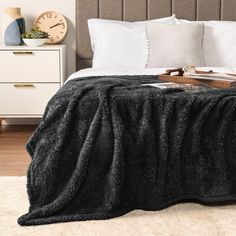 a bed with white pillows and black blanket on top of it next to a clock