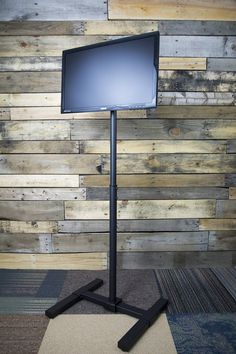 a computer monitor sitting on top of a metal stand in front of a wooden wall