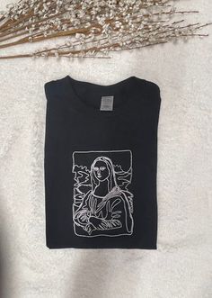 "The Outline of Da Vinci Mona Lisa embroidered on a regular style crewneck t-shirt. Perfect for someone interested in painting, art, artwork or just buy for a fun t-shirt to wear. It takes 1-2 weeks to make and process orders for shipping. If you require it sooner, you will need to purchase the \"rush order add-on\" Embroidered design will be as shown as in the picture. Please Pick Thread Color in Personalization Section. Item Description: Unisex Men Sizing Cotton and Polyester Pull On Short Sle Black Embroidered Crew Neck T-shirt, Black Cotton Tops With Machine Embroidery, Graphic Tee With Custom Embroidery Crew Neck, Embroidered Crew Neck Graphic Tee, Custom Embroidery Crew Neck T-shirt, Famous Portraits, Embroidered Design, Painting Art, Art Artwork