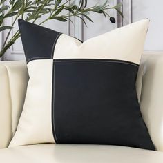 a black and white pillow sitting on top of a couch next to a potted plant