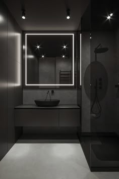 a black and white photo of a bathroom with lights on the mirror above the sink