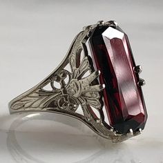 Details: Stunning Edwardian Period garnet and 14K white gold filigree ring! The stone measures 14.5mm by 7mm, and the is 4.6mm above the finger at the highest point on the ring. The filigree is beautiful on this ring, and is in lovely shape. This is a stunning ring--you will not be disappointed! Please ask all necessary questions prior to placing an order. Measurements: The size is 4 1/2 US and can be sized for a fee. Condition: The overall all condition of this ring is very good. Elegant Garnet Filigree Jewelry, Classic Garnet Rings For Wedding, Elegant Garnet Jewelry With Filigree Detail, Elegant Garnet Jewelry With Filigree, Ornate Hallmarked Amethyst Ring For Formal Occasions, Ornate Hallmarked Amethyst Ring For Formal Events, Formal Engraved Emerald Cut Ring, Vintage Sterling Silver Ruby Ring For Formal Occasion, Formal Emerald Cut Engraved Rings