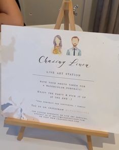 a white sign sitting on top of a table next to a wooden easel with an image of a man and woman