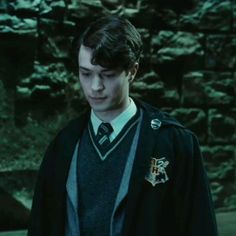 a young man in a harry potter outfit looking down at his cell phone while standing next to a stone wall