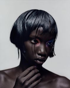 a woman with black hair and blue eyes poses for the camera, her hands on her face