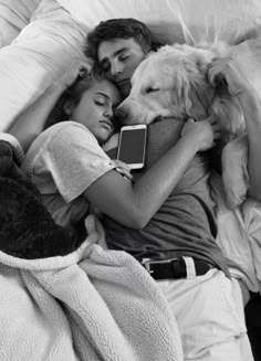 a man and woman laying in bed next to a dog with an electronic device on their lap