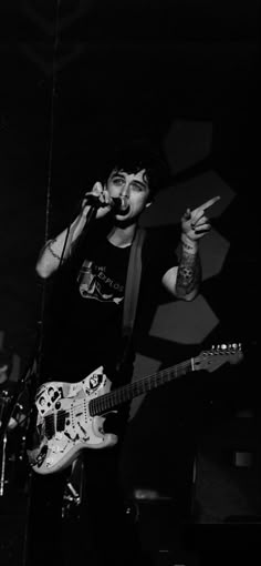 black and white photograph of a man singing into a microphone while playing an electric guitar