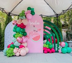 there is a pink and green arch with balloons on the top, and watermelon decorations around it