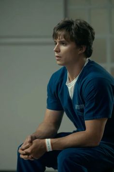 a young man sitting on top of a wooden bench in front of a white wall