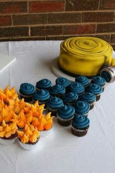 a table topped with cupcakes next to a yellow cake and blue frosted cupcakes