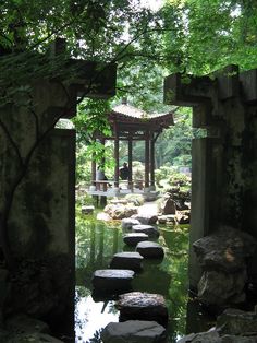 an open doorway leading to a small pond with stepping stones in the water and trees around it