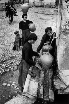 three women are filling water from a well in an old photo, while another woman stands nearby