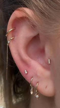 a woman wearing three different ear piercings on her left ear, and one with two dangling