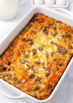 a casserole dish with meat and cheese in it on a table next to eggs