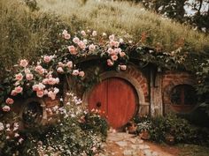 a red door surrounded by pink flowers and greenery on the side of a building