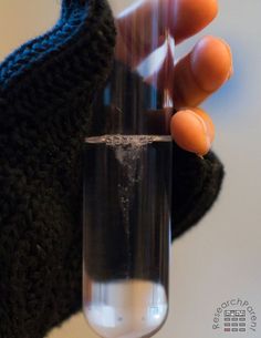 a hand holding a glass filled with water and an orange object in it's left hand