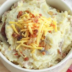 a white bowl filled with mashed potatoes covered in cheese and bacon on top of a red checkered napkin