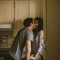 a man and woman kissing in the kitchen while sitting next to each other on the counter