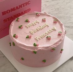 a pink birthday cake sitting on top of a table next to a card that says romantic standard