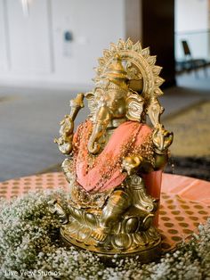 there is a gold statue sitting on top of a table with flowers in front of it