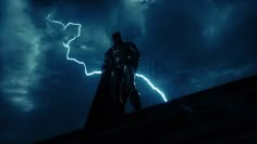 the dark knight standing on top of a roof with lightning in the sky behind him