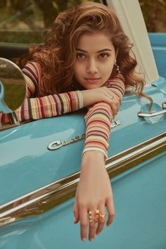 a woman leaning on the hood of a blue car with her hand resting on the door handle