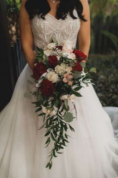 a woman in a wedding dress holding a bridal bouquet with red and white flowers