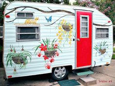 an old trailer painted with flowers and butterflies on it's side is parked in front of a house