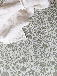 an unmade bed with white sheets and green floral designs on the sheet coverlet