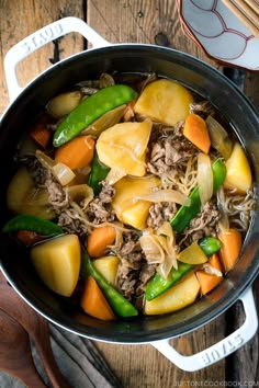 a pot filled with meat and vegetables on top of a wooden table