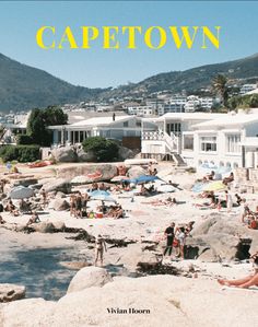 people are on the beach and in the water near some houses with yellow lettering that reads cape town