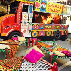 a brightly colored food truck parked in front of a building with tables and chairs around it