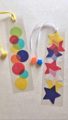 two bookmarks made out of colored paper and string with star shapes on them next to each other